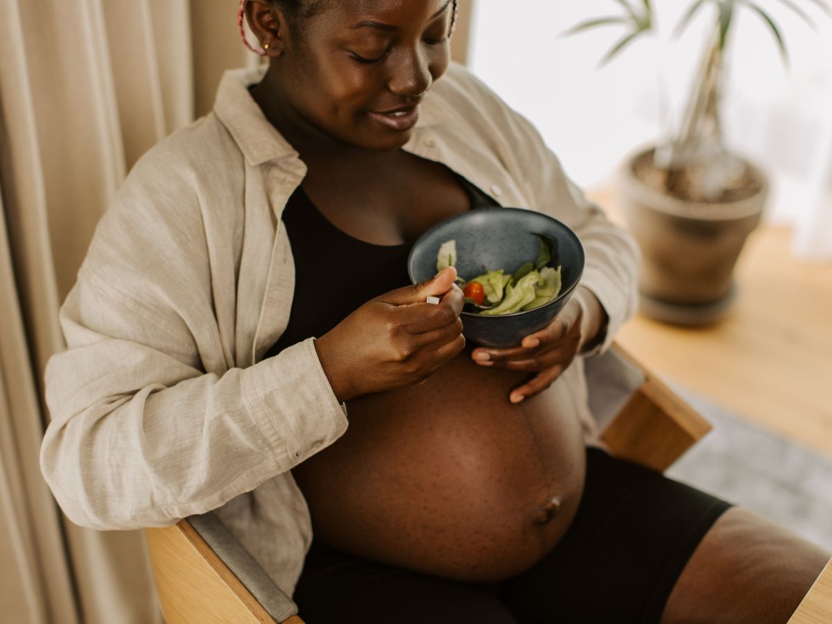 Pregnanct woman can be seen eating out of a bowl. Improving Maternal Health: How Our Pregnancy Meal Plan Benefits You